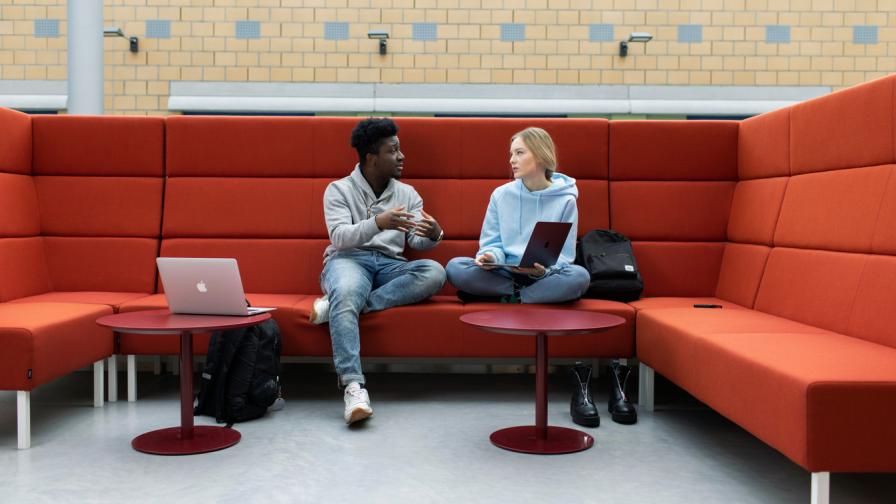 Kaksi ihmistä keskustelee sohvaryhmällä istuen